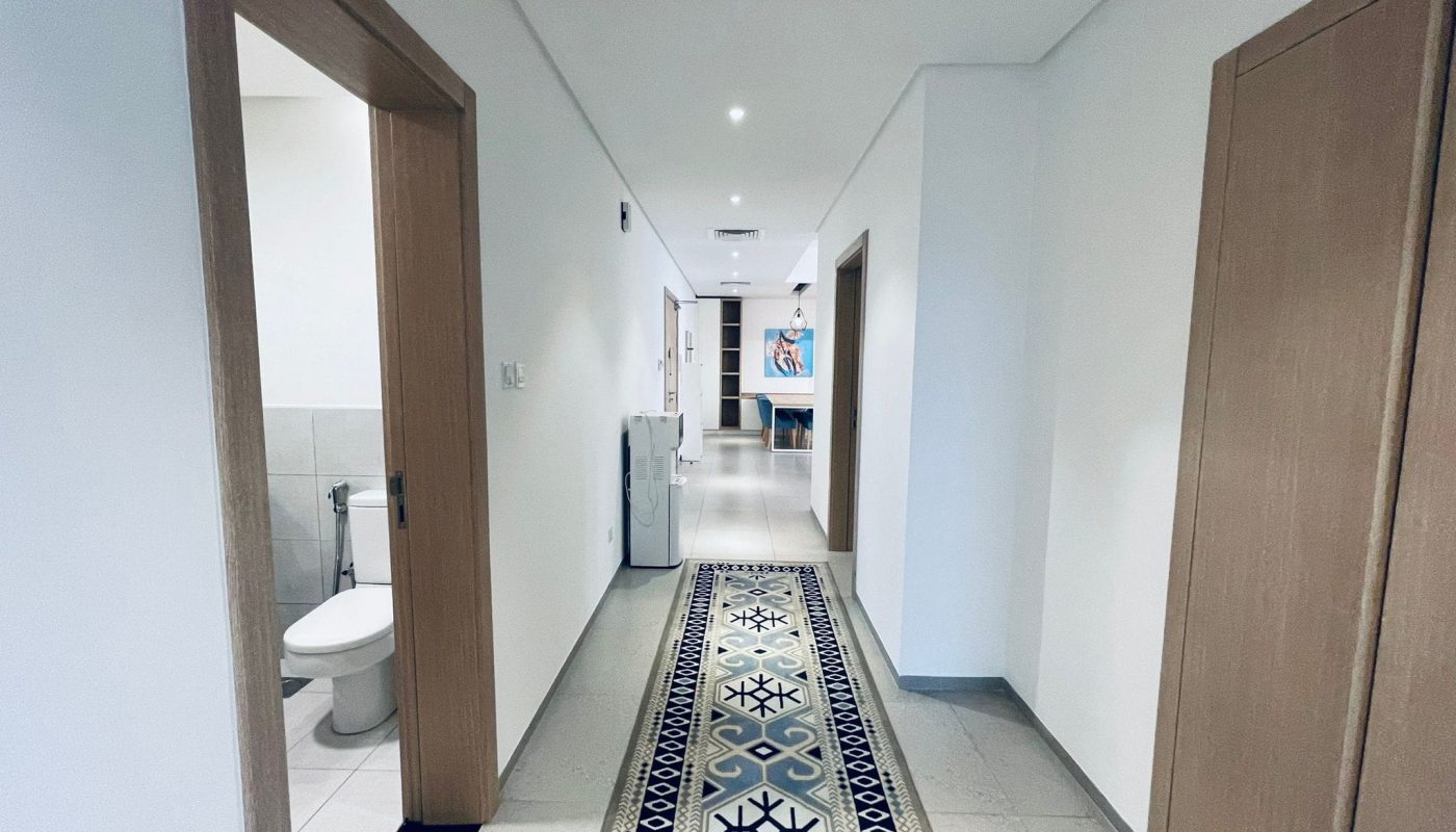 A hallway in a modern building with an ornate floor runner, open doors leading to a bathroom on the left and other rooms on the right. Auto Draft