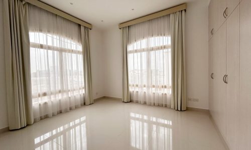 Bright, empty room with glossy tiled floor and windows draped with sheer curtains.