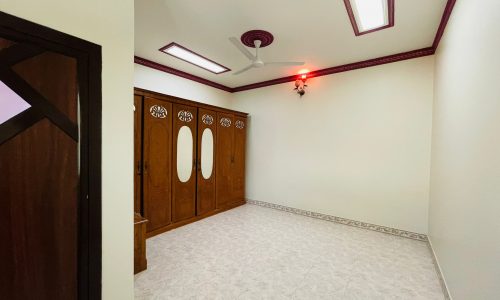 An empty 2BR Villa in Ras Rumman with white tiled flooring, off-white walls with decorative borders, a ceiling fan, and a wooden double door closet.