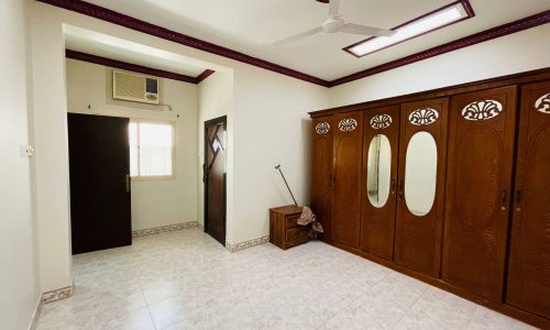 A spacious, well-lit 2BR Villa in Ras Rumman with tiled flooring, traditional wooden doors, a ceiling fan, and an air conditioning unit.