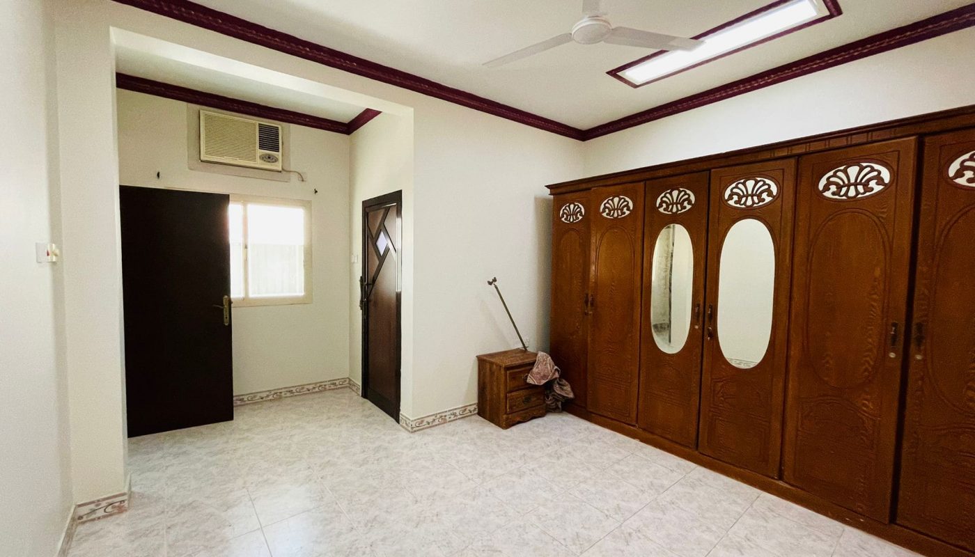 A spacious, well-lit 2BR Villa in Ras Rumman with tiled flooring, traditional wooden doors, a ceiling fan, and an air conditioning unit.