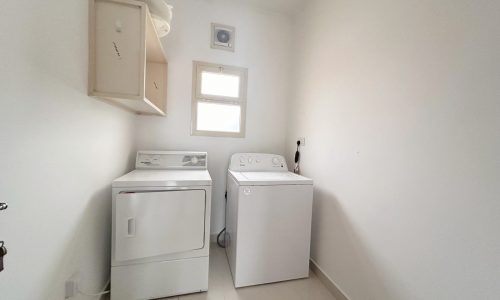 A small, bright laundry room with a top-load washing machine and a dryer side by side under an Auto Draft.