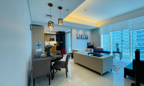 Modern apartment interior in Juffair with open-plan living and dining area, featuring contemporary furniture and lighting, with large windows overlooking a cityscape. This luxury 2BR apartment combines elegance with functionality.