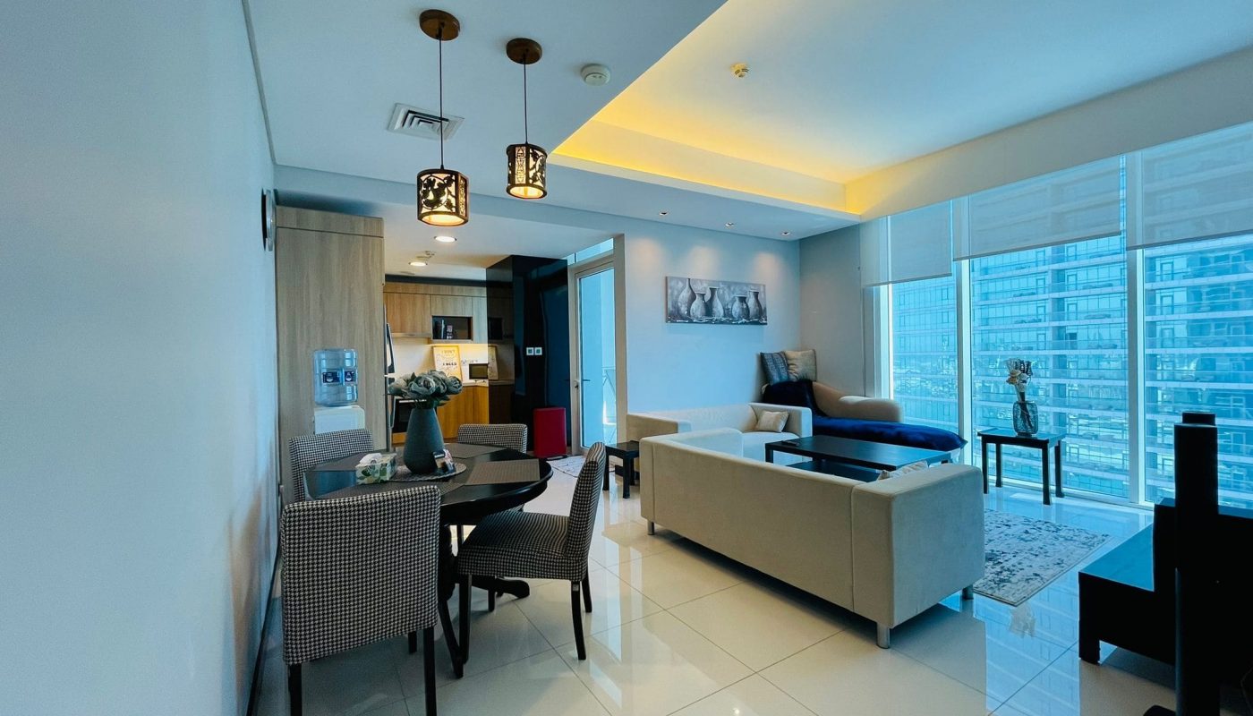 Modern apartment interior in Juffair with open-plan living and dining area, featuring contemporary furniture and lighting, with large windows overlooking a cityscape. This luxury 2BR apartment combines elegance with functionality.