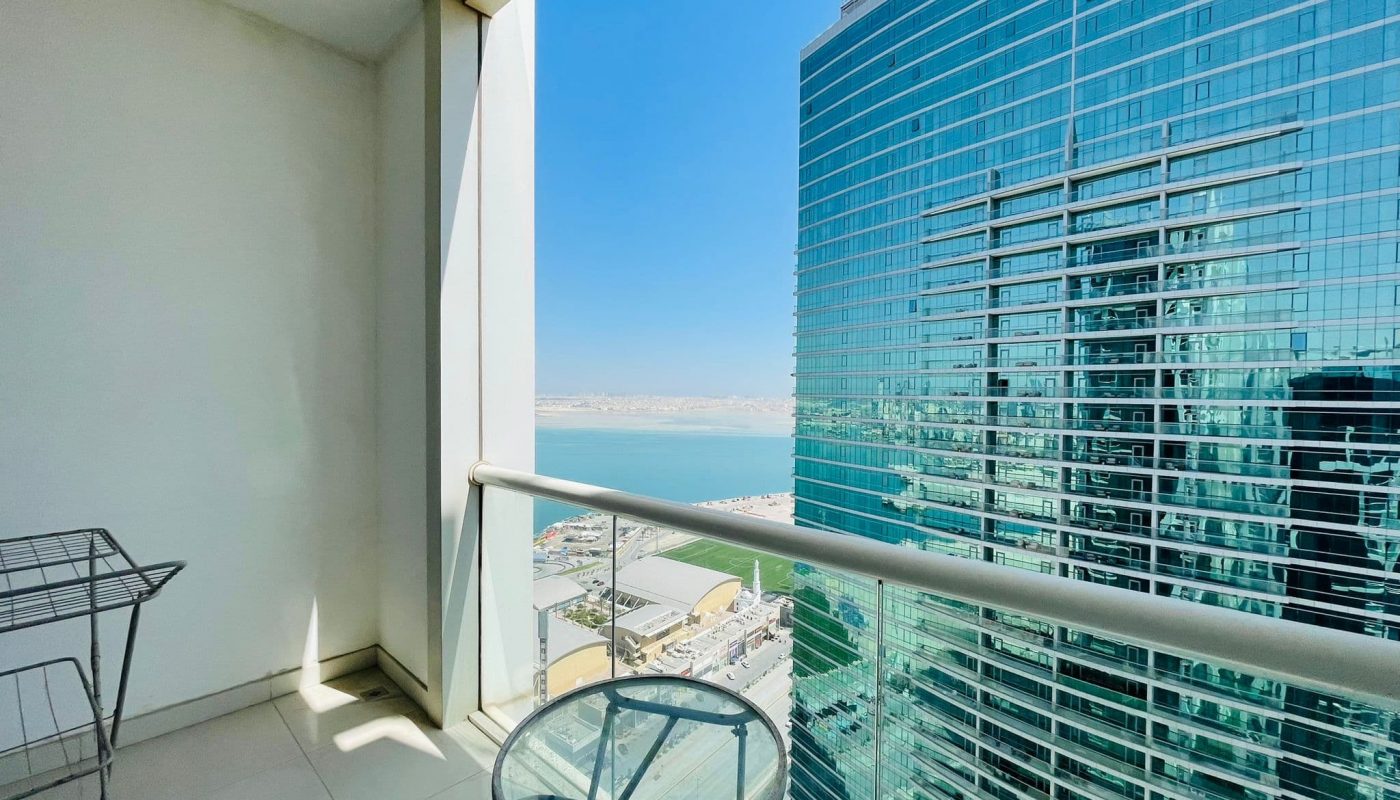 Luxury 2BR apartment with high-rise balcony view overlooking urban structures in Juffair and a distant waterfront.