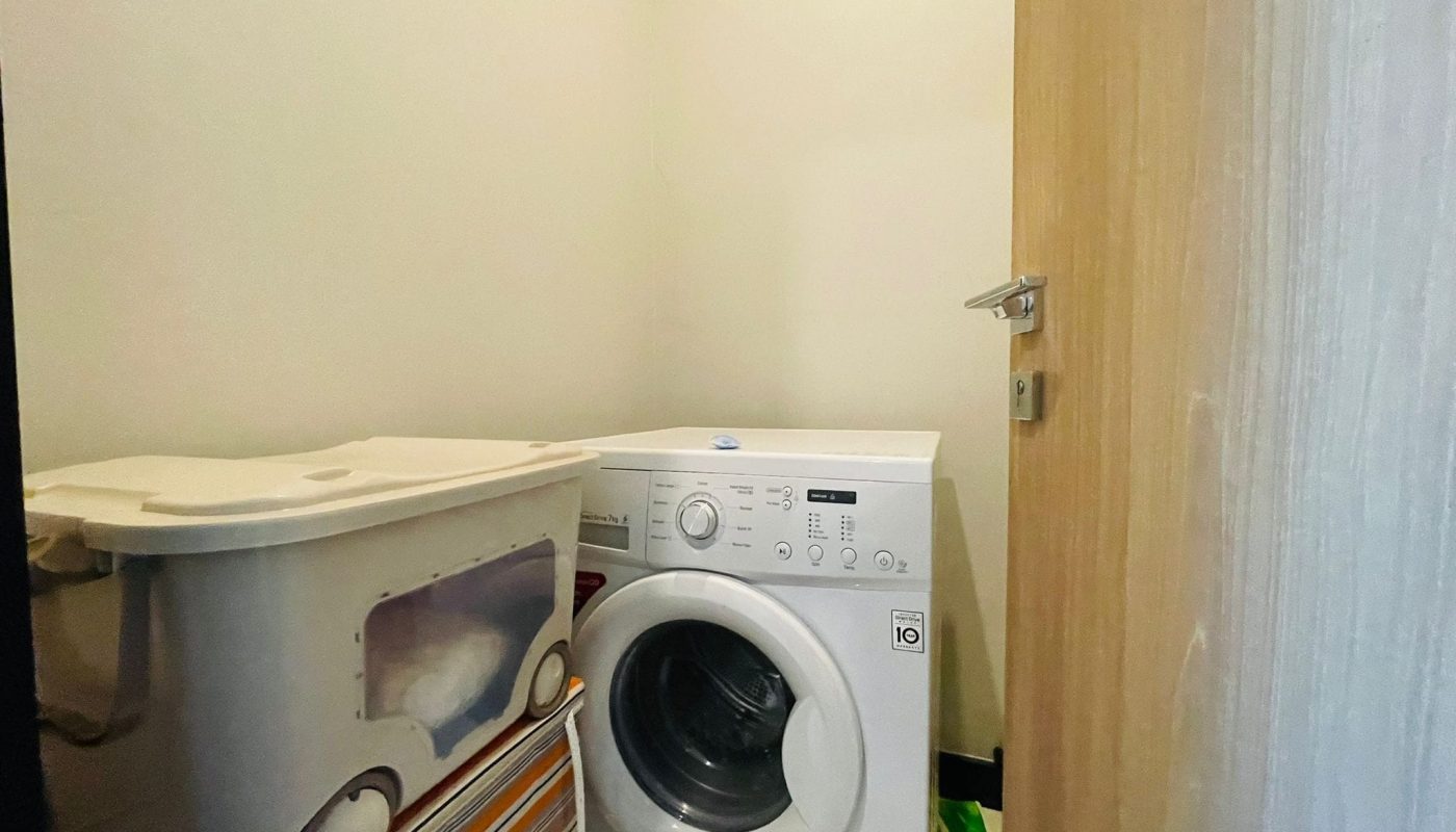 A laundry room in a luxury 2BR apartment in Juffair, with a white washing machine and a laundry basket.