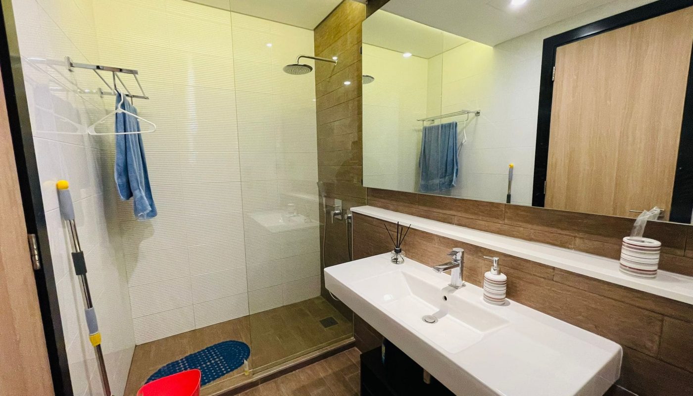 Modern bathroom interior in a luxury 2BR apartment with a walk-in shower, double sink vanity, and large mirror.