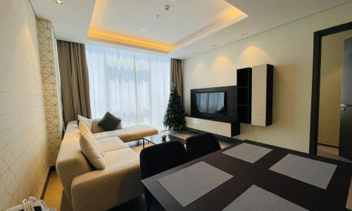 Modern living room with a beige sofa, a flat-screen tv, and a dining area with a black table set for four.