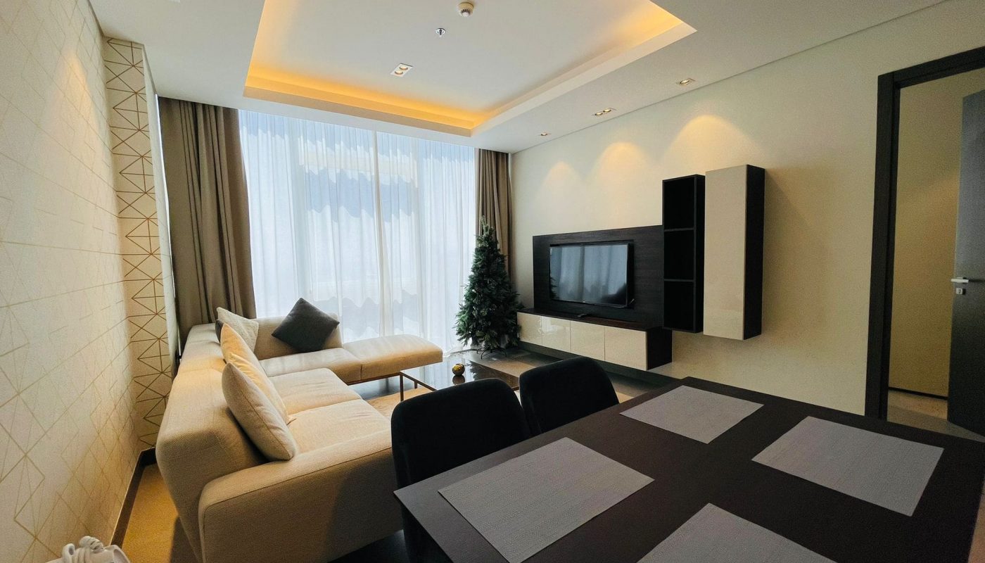 Modern living room with a beige sofa, a flat-screen tv, and a dining area with a black table set for four.