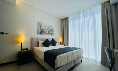 Modern bedroom with a large bed, side lamps, and sheer curtains.