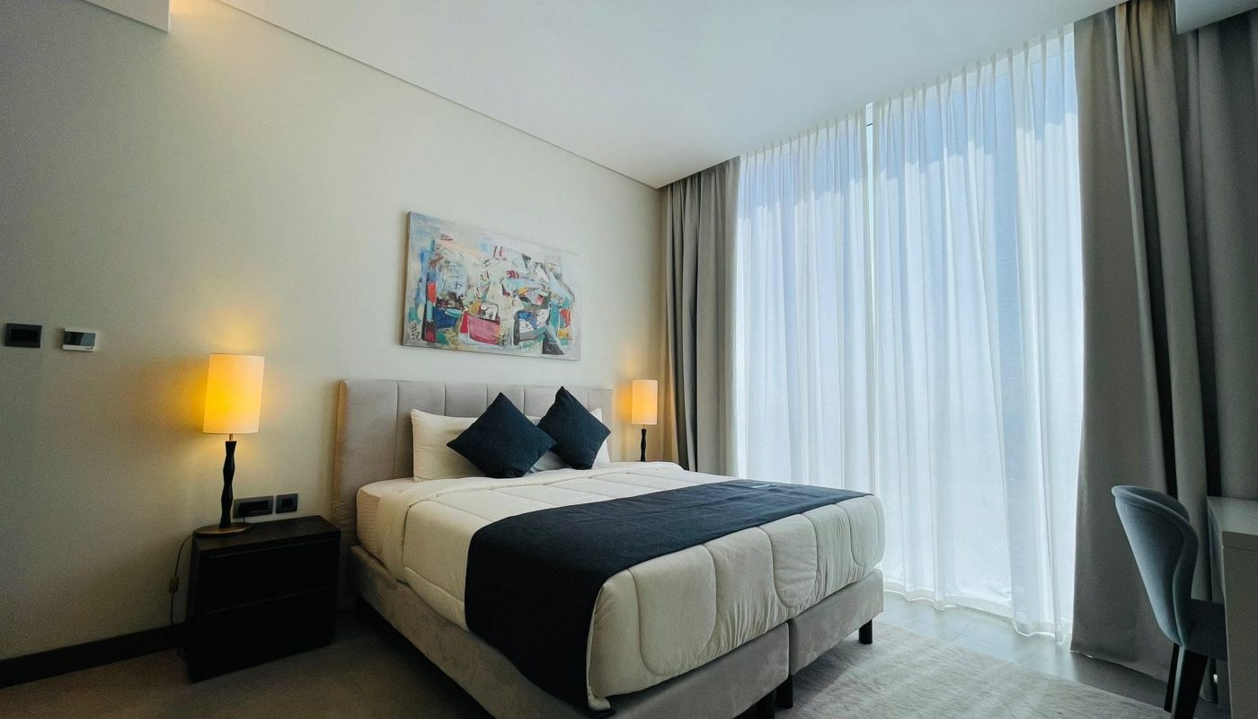 Modern bedroom with a large bed, side lamps, and sheer curtains.