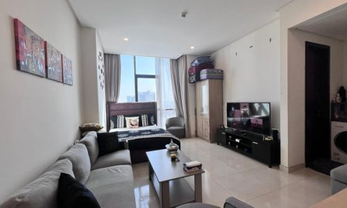 Modern living room in a Juffair flat for sale with a gray sectional sofa, tv stand, and city view from the window.