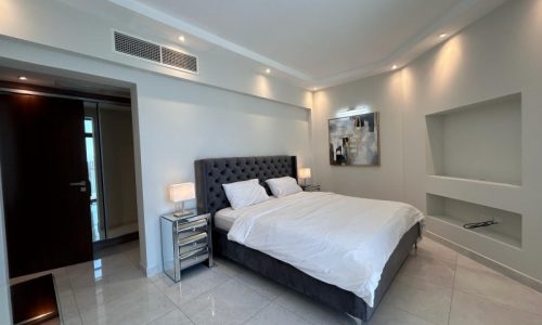 Modern bedroom interior in a luxury furnished apartment with a large bed, side tables, and minimalist decor.