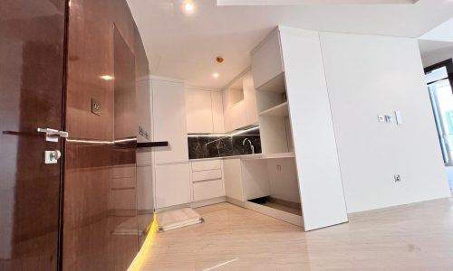 A modern, empty kitchen interior with white cabinetry and wooden flooring, overlooking the serene Bahrain Water Bay Sea in a brand new apartment.