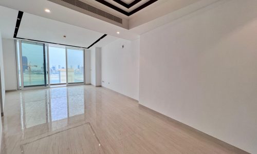 Empty apartment in Bahrain with glossy tiled flooring, white walls, and a large window overlooking the Water Bay Sea, letting in natural light.