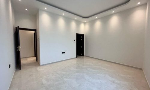 An apartment for rent in the Janabiyah area, featuring an empty room with white walls, recessed lighting, and marble flooring with doors leading to other areas.