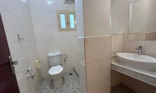 A clean and compact bathroom with a toilet, bidet, sink, and shower area in an Apartment Janabiyah, tiled in a light color scheme.