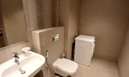 Modern bathroom interior with beige tiles, featuring a white toilet, sink, auto draft, and a small cabinet.