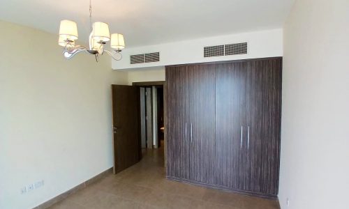 An empty room with tiled flooring featuring a large wooden wardrobe, an Auto Draft, and a chandelier.