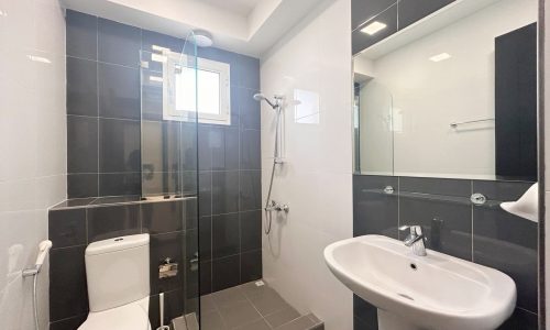 A modern bathroom with a glass shower enclosure, toilet, and pedestal sink. Auto Draft.