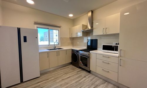 Modern kitchen interior in a fully-furnished apartment with white appliances and cabinetry.