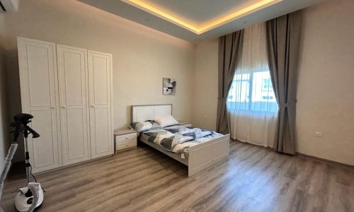 Modern 2 BDR apartment bedroom with a double bed, wooden flooring, white wardrobe, and a scooter near the door.