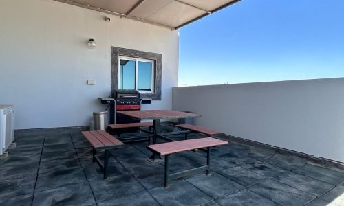 Outdoor rooftop patio in a luxury apartment for rent, featuring a picnic table and a barbecue grill.