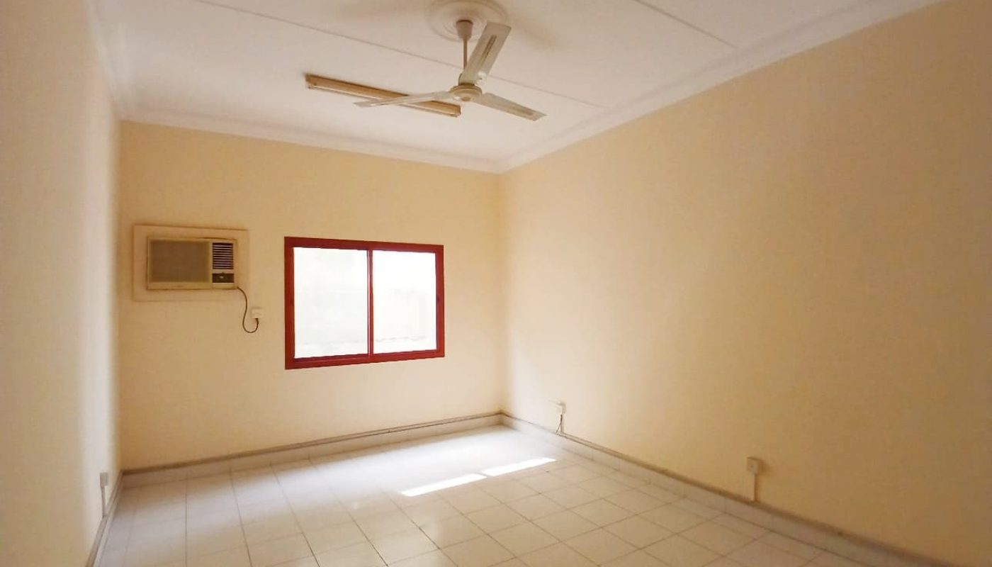 A bright and empty room with a ceiling fan, air conditioning unit, and a large window with red trim awaits its Auto Draft.