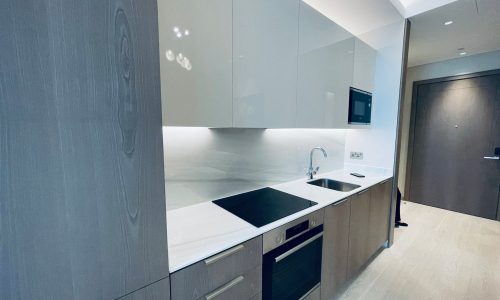 Modern kitchen interior with gray cabinets, white countertops, and built-in appliances in an amazing apartment for rent in Seef.