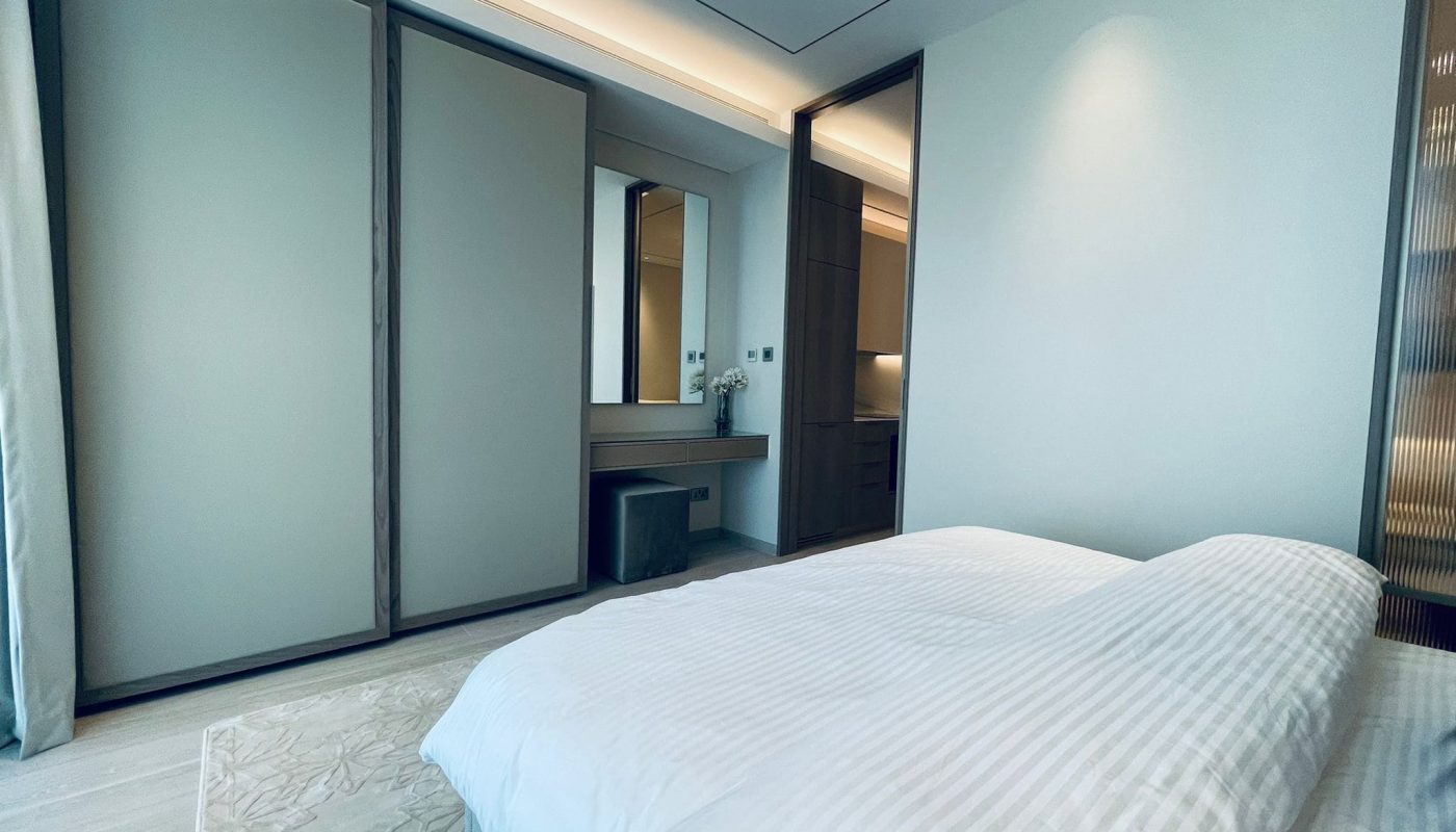 An amazing apartment featuring a modern bedroom with a large bed adorned in white bedding, sliding wardrobe doors, and a vanity area.
