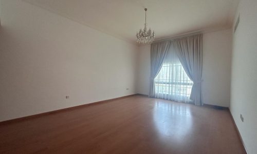 Empty room with hardwood flooring, a chandelier, and a large window with auto draft curtains.