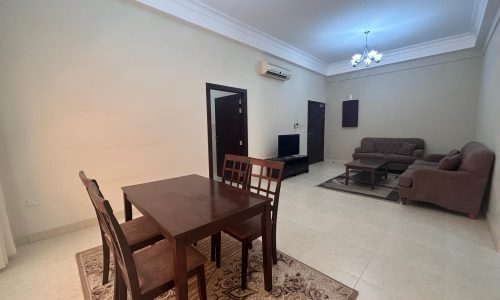 A well-lit, spacious living room in a luxury Saar apartment with minimal furniture including a dining table, chairs, sofas, and a television set.