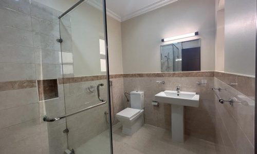 A modern bathroom interior in a luxury apartment featuring a glass shower enclosure, a wall-mounted sink, and a toilet.