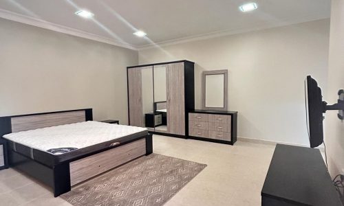 A modern bedroom with a large bed, a wardrobe, a dresser with a mirror, and Auto Draft on a stand, featuring tiled flooring and recessed ceiling lights.