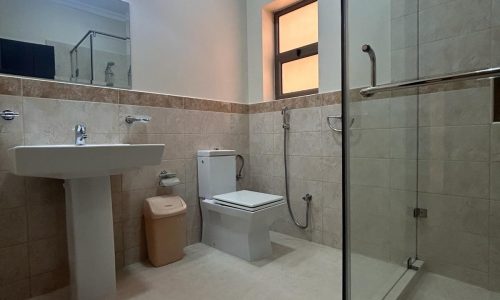 A clean, modern Auto Draft bathroom with beige tiles featuring a sink, toilet, and glass-enclosed shower area.