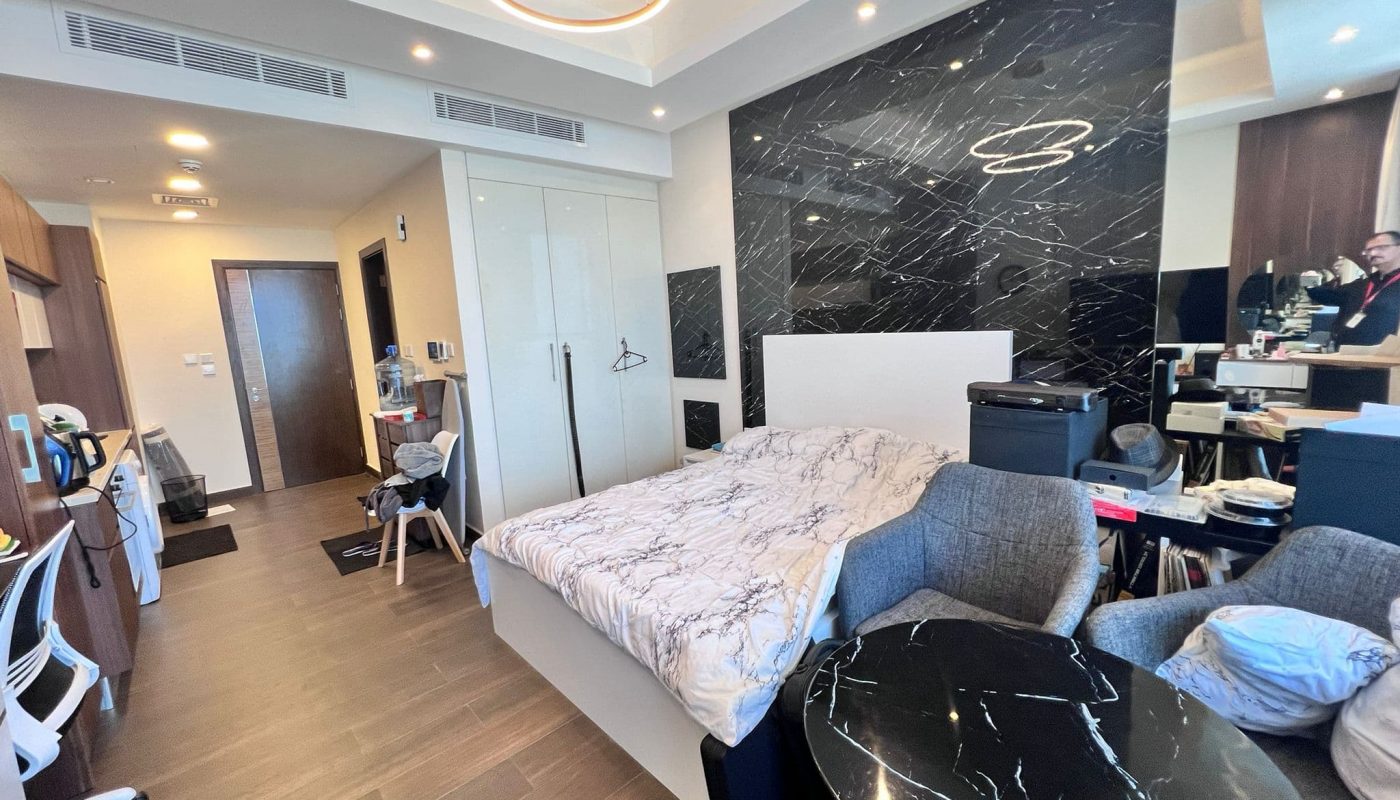 Modern bedroom in a luxury flat with a large bed, dark marble accents, circular lighting fixture, and an open entrance area.