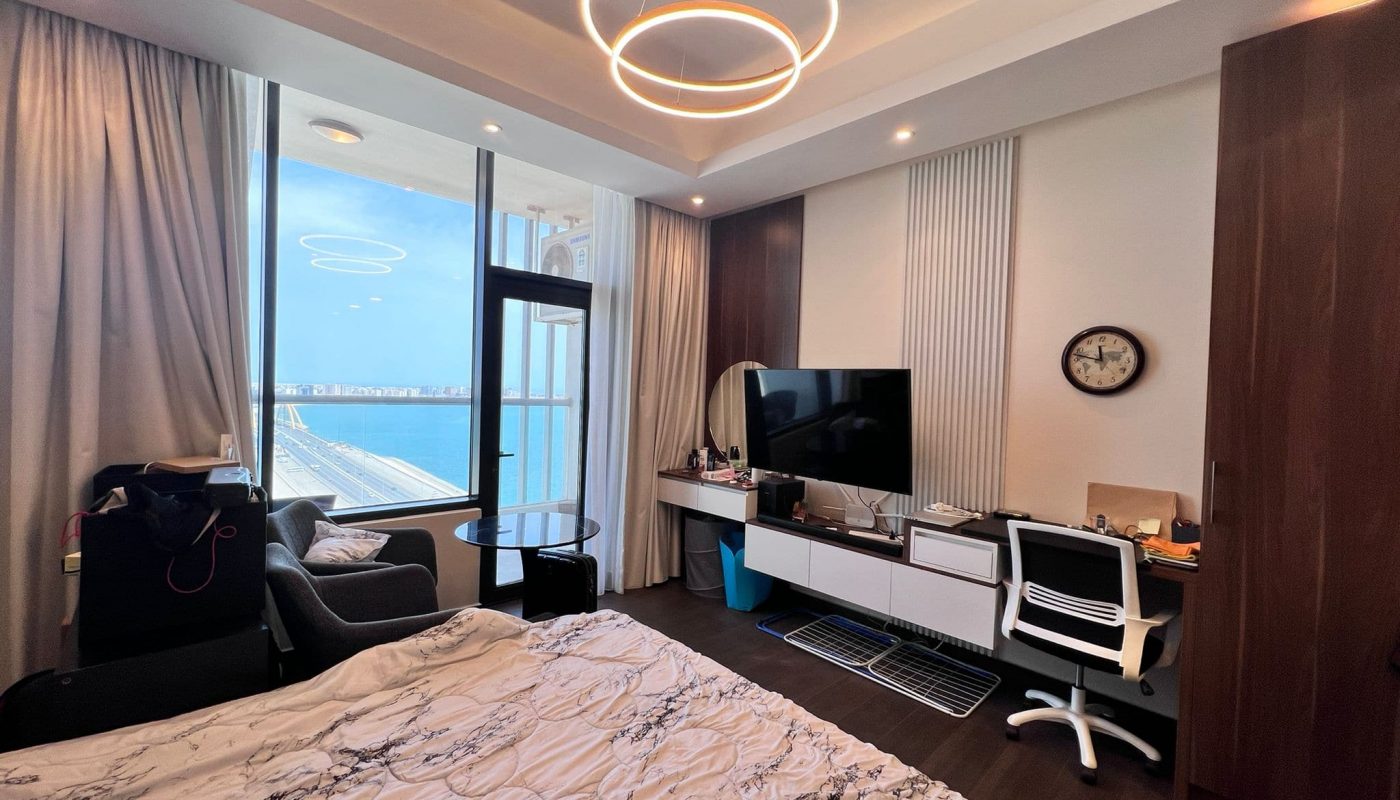 Modern bedroom in a luxury flat in Juffair with a large bed, desk area, and a view of the water through the balcony door.