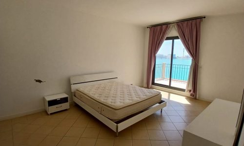 Minimalist 3BR Villa Amwaj bedroom with an unmade bed facing a window overlooking the sea.