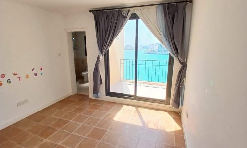 A bright, unfurnished room in a 3BR Villa Amwaj with an open balcony door revealing a view of the sea.