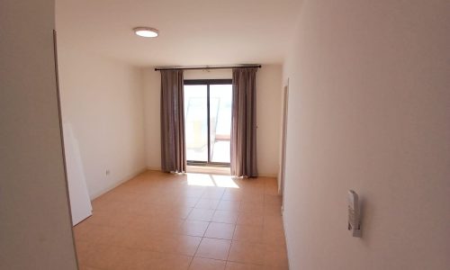 A bright, empty seafront villa room with tiled floor, a window with curtains, and a closed door.