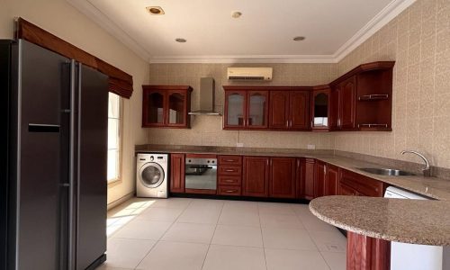 Modern kitchen interior with wooden cabinets, stainless steel appliances in a 3 BDR fully-furnished villa for rent in the Saar area includes a washing machine.