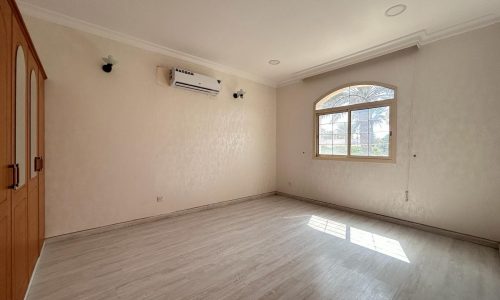 Empty room with beige walls, wooden flooring, arched window, and an air conditioner unit mounted on the wall.