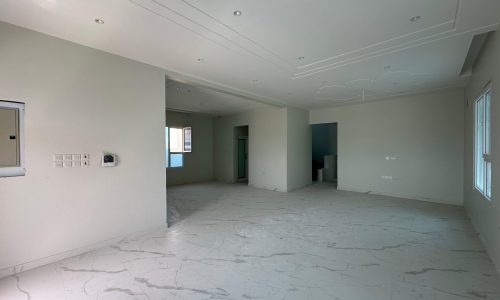 Spacious empty room with white marble flooring, light gray walls, and various light fixtures on the ceiling.