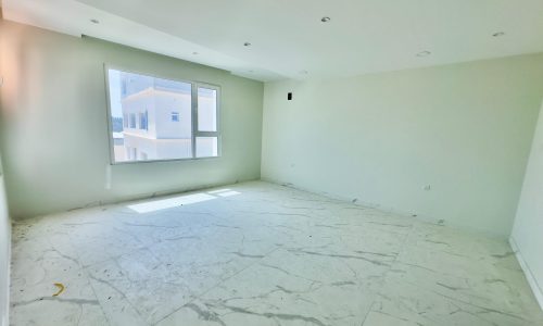 Empty room with white marble flooring and white walls, featuring a large window with a view of neighboring buildings.