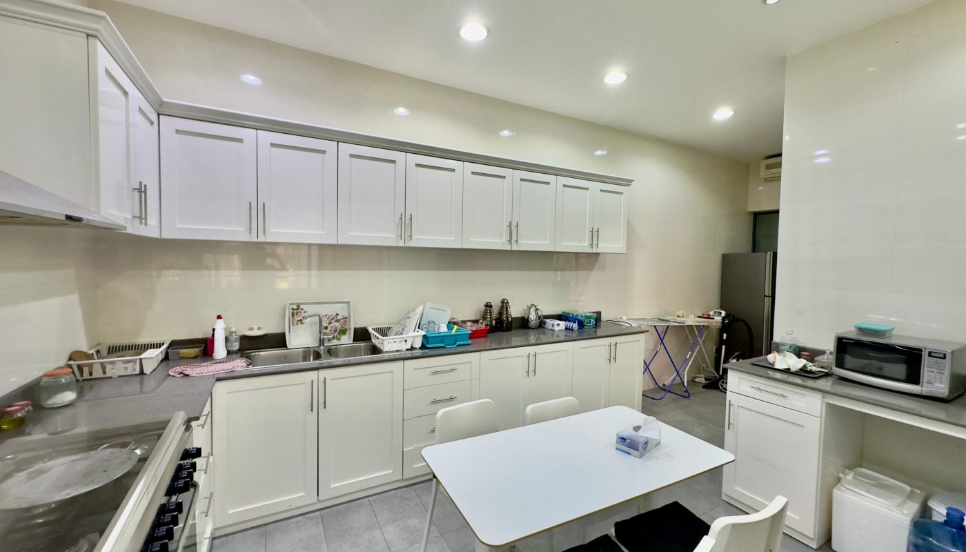 A modern kitchen with white cabinets, gas stove, and a center island, featuring a table with chairs and various household items scattered throughout.