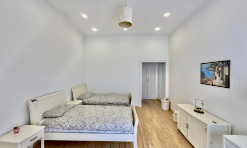 A bright, modern bedroom with a double bed, patterned bedding, white furniture, and recessed lighting. a framed picture hangs on the wall.