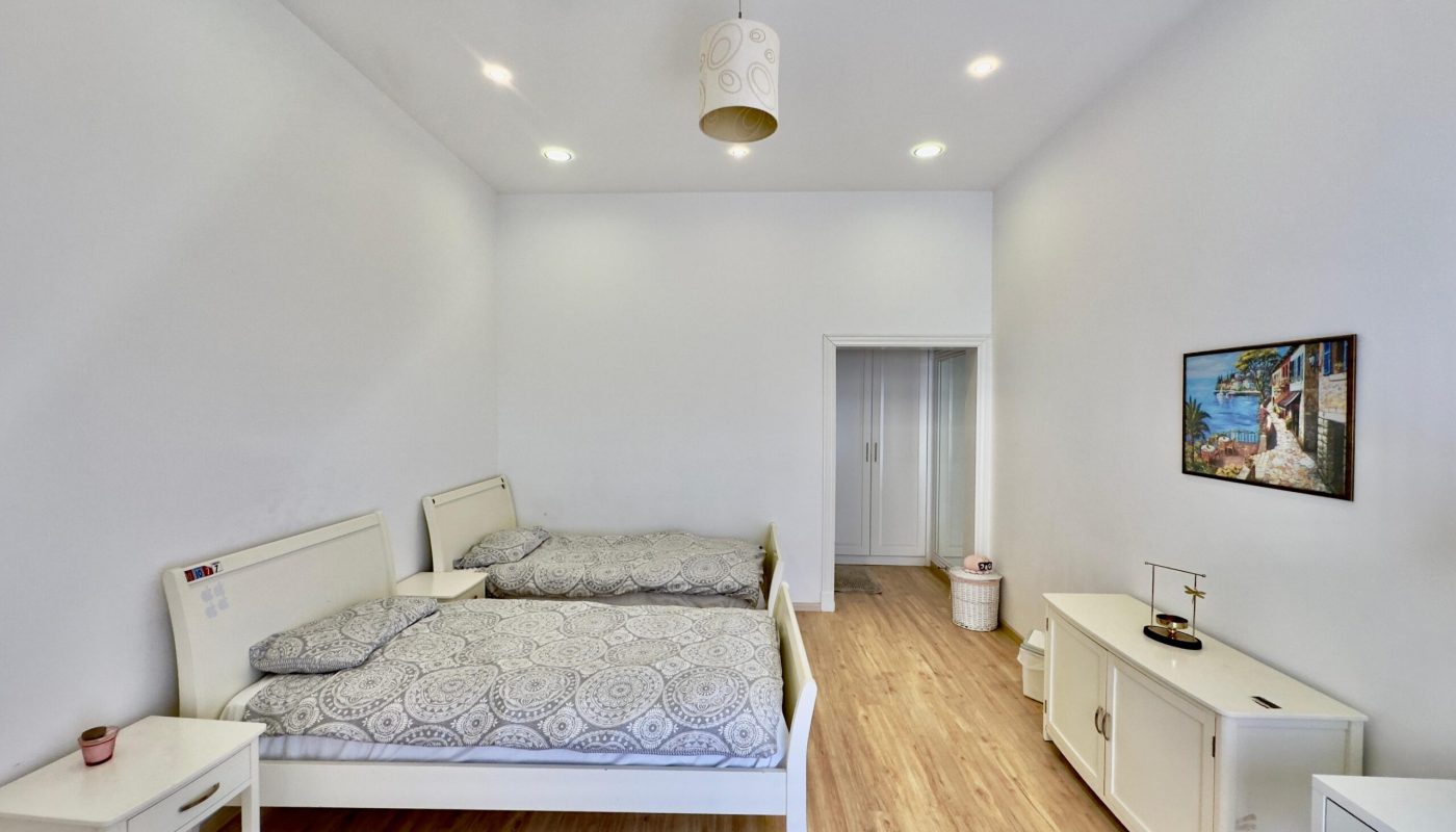 A bright, modern bedroom with a double bed, patterned bedding, white furniture, and recessed lighting. a framed picture hangs on the wall.