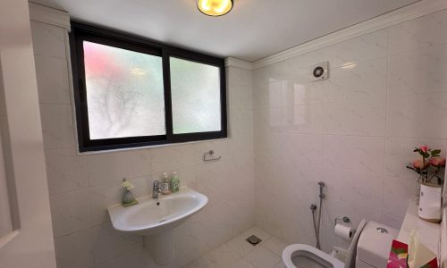 A clean bathroom with white tiled walls, featuring a toilet, a sink, and a frosted window with a small open panel.