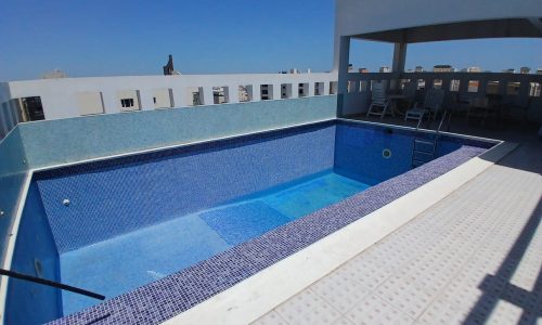 Rooftop pool surrounded by a white deck in the Al Hidd area, under a clear blue sky.