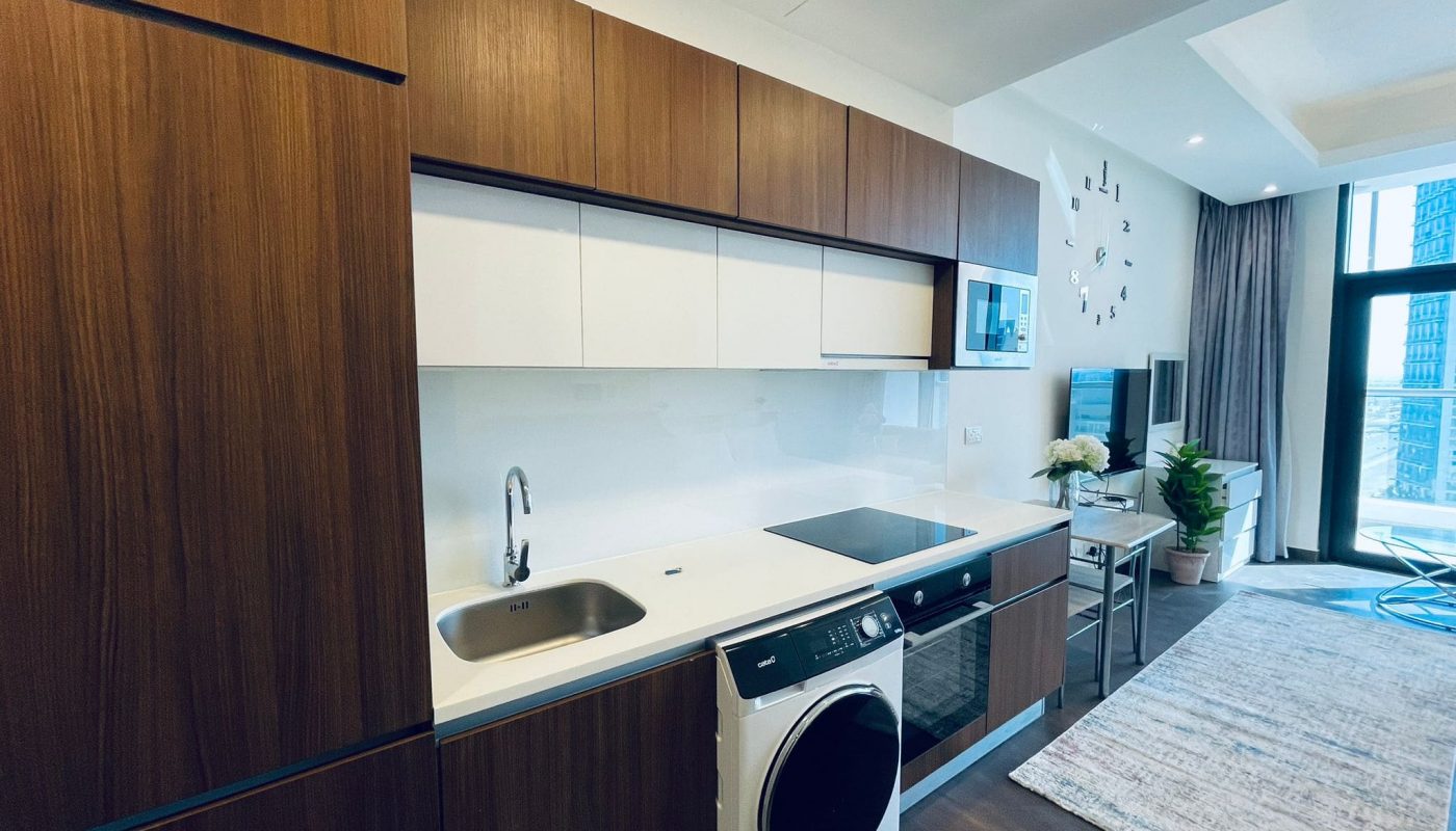 Luxury studio kitchen interior with wooden cabinets, white appliances, and a view of the city through large windows.